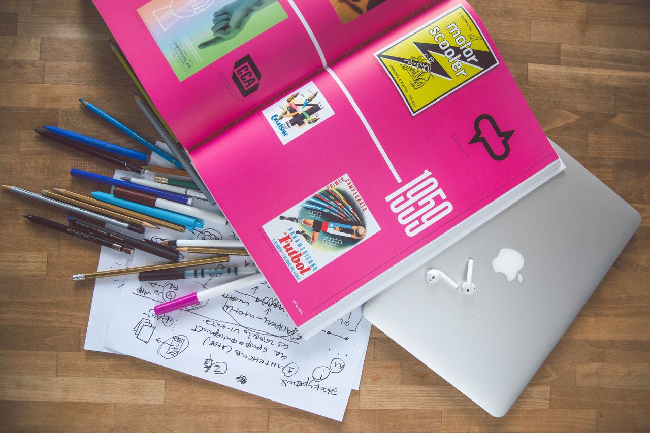Un bureau lumineux et soigné avec un livre de design, un ordinateur portable et des outils créatifs, parfait pour nourrir l’inspiration.
